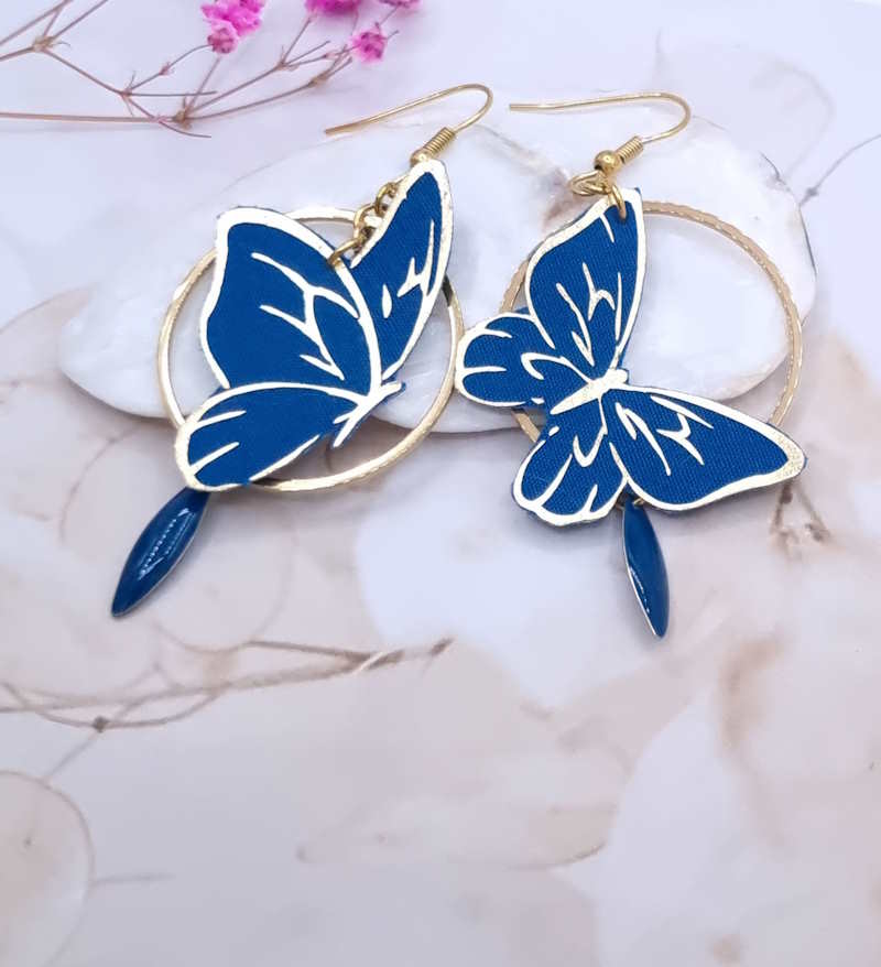 Affirmez votre style avec l'éclat des boucles d'oreilles "Papillon Saphir". Un duo graphique et coloré, alliant la noblesse du bleu cobalt à une structure dorée contemporaine.